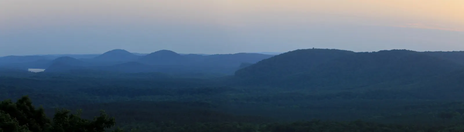 Rounded, forested Uwharrie Mountain peaks fading into blue haze at dusk, with a glimpse of Lake Tillery on the left